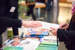Exhibitor sharing a pamphlet with a conference attendee